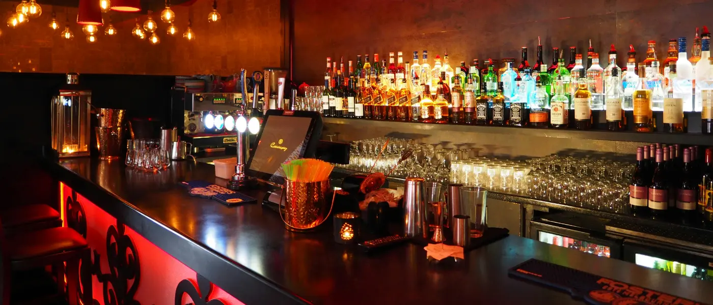 Bar Management Guide - A dark bar counter with a line of alcoholic drink bottles on shelves behind the bar