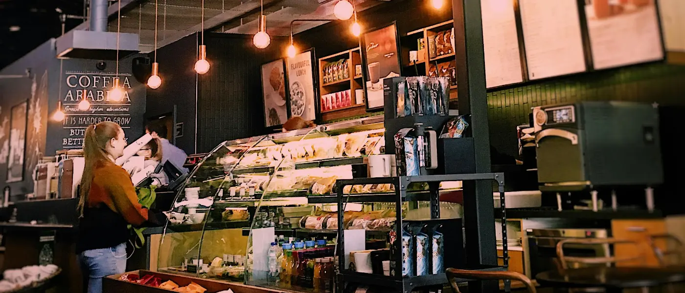 How to open a successful cafe in the UK - a woman stands at the cafe counter, which is full of sandwiches, drinks, and pastries.